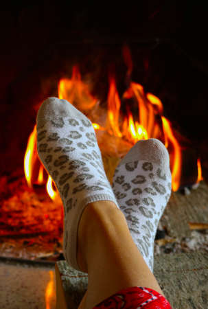 Burning wood at the fireplace, female legs in socks warming up. Firewood bricks at the fire, woman foot heating.の写真素材