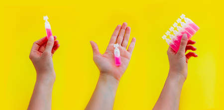 Female hand holding pink liquid medicine in an ampoule, isolated on yellow background.の写真素材