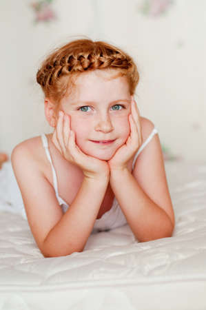  Little girl with red hair in a white dress on the bedの写真素材