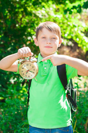 boy with a backpack and a clock in hands on nature