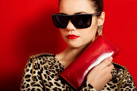 Beautiful girl in a trendy dress and red clutch with sunglassesの写真素材