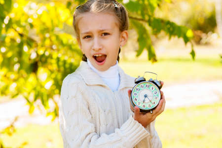 Little girl with a clock in his hands in the park in autumnの写真素材