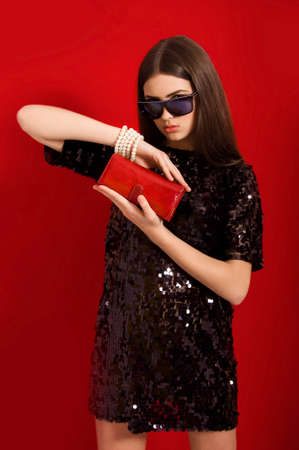 Beautiful young girl in a black dress and sunglasses with red purse