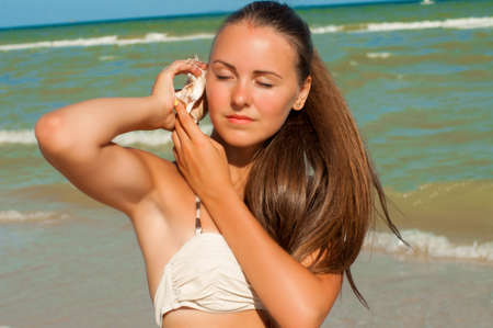 Young girl with long hair in a bikini on a beach with shell in handの写真素材