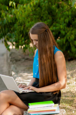 Teen girl works with the laptop in headphones and bookの写真素材