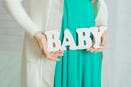 Belly of a pregnant woman in a turquoise dress with a sign babyの写真素材
