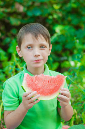 Little boy eating watermelon in the summer in the gardenの写真素材