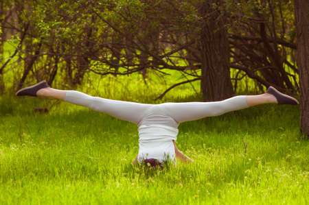 Young girl doing yoga on a green grass in summer