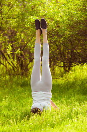 Young girl doing yoga on a green grass in summer