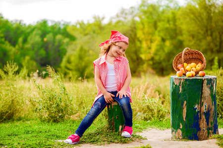 Little girl in jeans and a shirt near a river in autumn with applesの写真素材