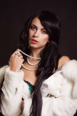 Beautiful girl with dark hair in a white fur coat with pearls