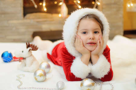 Little girl dressed as Santa by the fireplace at homeの写真素材
