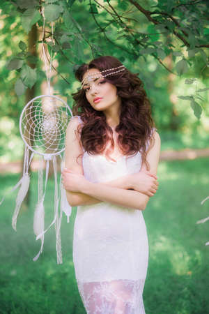 Beautiful girl with long curly hair in a white dress in a summer park. Girl with the Dreamcatcher in the summer parkの写真素材