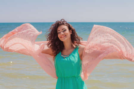 Young girl on the beach in summer in a beautiful dress with a flying scarf in handsの写真素材