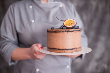 chocolate cake on a dark background adorned with nuts. The confectioner's hand holds a piece of cake on the patisserie.の写真素材