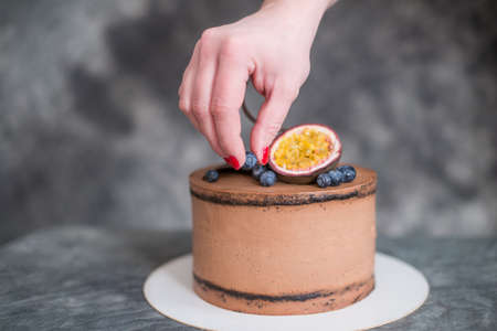 chocolate cake on a dark background adorned with nuts. The confectioner's hand holds a piece of cake on the patisserie.の写真素材