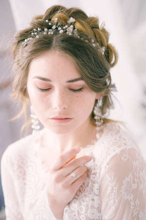 Portrait of beautiful bride. Morning of the bride. Wedding morning. Makeup. Bride with cones and fair hair. Fragile bride in white lace negligeeの写真素材