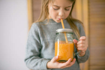 Cute little girl with glass of orange juice at home, closeupの写真素材