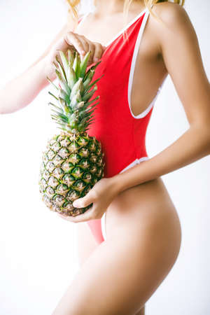 Portrait of young woman in swimsuit with pineapple on white background. Summer season image conceptの写真素材