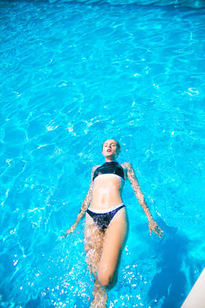 Beautiful girl with swimsuit pays in the outdoor pool in summer
