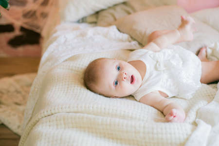 Cute little baby girl in white clothes lying at home on the bed and smilingの写真素材