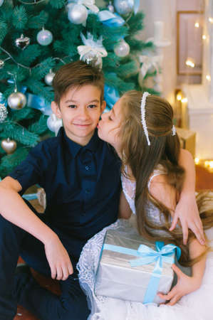 Children, a boy and a girl in a white ball gown near a Christmas tree in holiday dresses with gifts and silver confetti. Christmas moodの写真素材