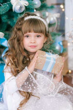 Cute girl with long hair in a white ball gown by the Christmas tree in holiday dresses with gifts and silver confetti. Christmas moodの写真素材