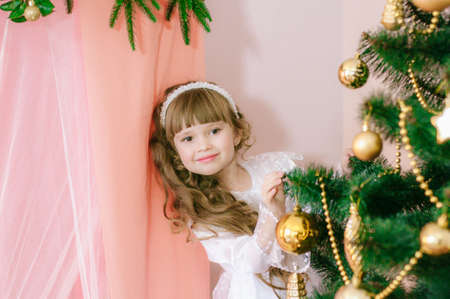 Cute girl with long hair in a white ball gown by the Christmas tree in holiday dresses with gifts and silver confetti. Christmas moodの写真素材
