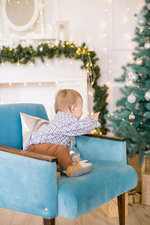 Cute little boy by the Christmas tree and fireplace decorated with garlands and gifts. Christmas moodの写真素材