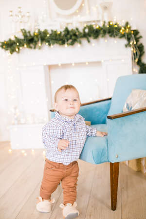 Cute little boy by the Christmas tree and fireplace decorated with garlands and gifts. Christmas moodの写真素材