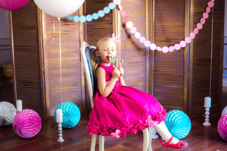 Little cute girl with blond hair in a pink dress and a princess crown with large bright balloons and garlands. Children's holiday. Children's decor. Balloonsの写真素材
