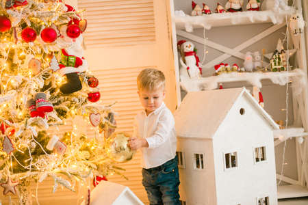 Cute little boy with blond hair plays with toys in a bright room decorated with Christmas garlands near the Christmas tree. Happy childhood. Christmas moodの写真素材