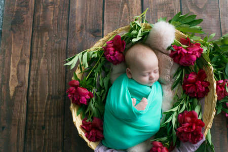 Baby girl in a wicker basket of vine decorated with  burgundy peonies   pink fur in a mint blanket . Spring photo. Flowers and children. Happy motherhoodの写真素材