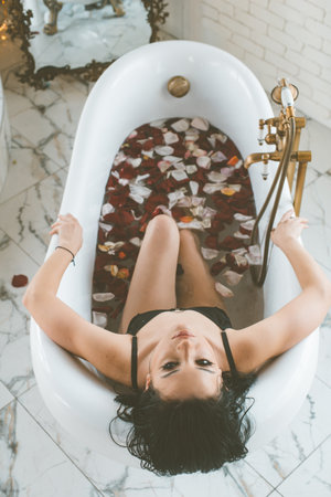 Attractive young girl with dark hair in a black bikini in a bathtub full of rose petals. Leisure & Spaの写真素材