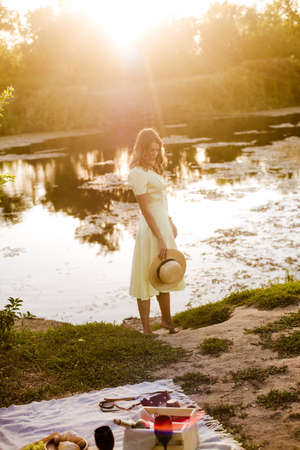 Young attractive girl with dark hair in a yellow summer dress by the river in summer at sunset. Healthy life.の写真素材