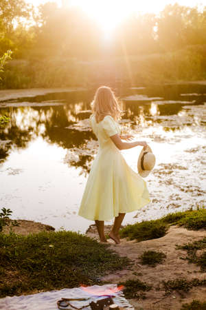 Young attractive girl with dark hair in a yellow summer dress by the river in summer at sunset. Healthy life.の写真素材