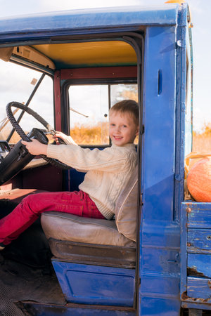 Little cute boy with blond hair in a white cozy knitted sweater on a pumpkin farm in autumn in the trunk of a truck among orange pumpkins. halloween. autumn vegetables. Thanksgivinの写真素材