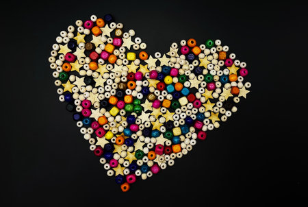 Wooden beads with colorful texture on a yellow background. A decorative accessory for handmade heart-shaped jewelry. A diverse concept of making handicrafts from natural materials. Close-up, layout, top view. A heart made of beadsの写真素材