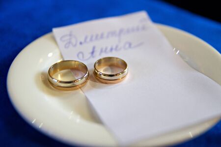 Wedding golden rings for a man and a woman on a plate with a note with their namesの写真素材
