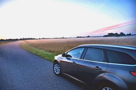 Asphalt road with a parked car in the morning mist on the background of dawn.の写真素材