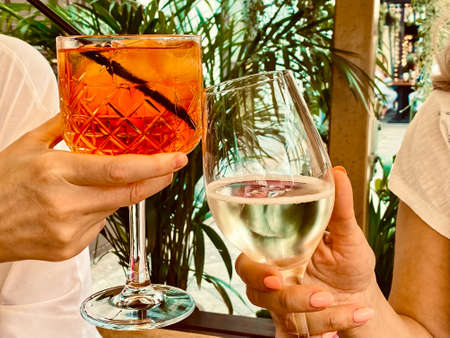 Two girls clinking glasses with aperol coctail and white wineの写真素材