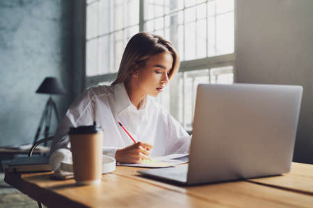 Girl sitting concentrated at laptop and studying remotely. Student using online opprotunities for...