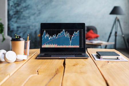 Closeup of laptop with stock market analyst monitor and cups, headphones, coffee on a table in a cafe. Freelancer home office. Workspace student distance learning. Work remotely. Online learning.の写真素材