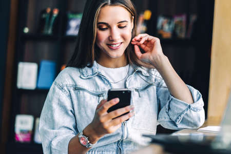 Business woman sits at table, holds smartphone in her hands, writes messages, conducts business...