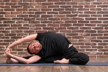 Sporty attractive young man working out, yoga, pilates, fitness training, asana Parivrtta Janu...