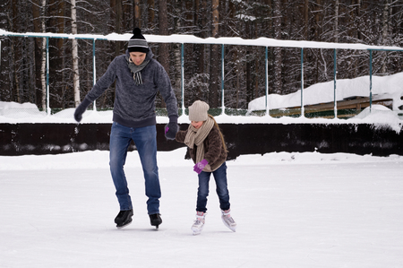Father and daughter in casual wear skating and play on ice rink together. Cold winter dayの写真素材