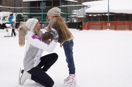 Smiling young mother and her cute daughter ice skating together. Family skating and training with white skates on the ice area in winter day. Weekends activities outdoor in cold weatherの写真素材