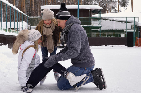 A little girl with his parents skates on the outdoor ice rink in the winter. Active family sport, winter holidays, sports clubsの写真素材