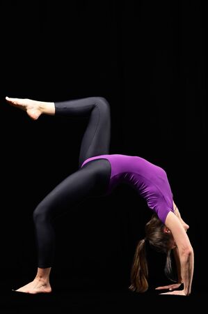 Beautiful young fit woman with slim muscular body in sportswear doing yoga exercise. Full length, side view, studio shot, black backgroundの写真素材