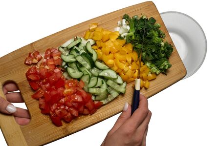 Top view of process of cooking vegetarian salad. Sliced vegetables: tomato, cucumber, paprika, green onion, dill and parsley sprinkle from cutting board to glass bowl. Healthy foodの写真素材